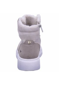 Botte de cheville en suède beige clair avec une doublure en peluche, semelle blanche et un bouton rond doré décoratif sur le côté. Comprend une fermeture éclair.