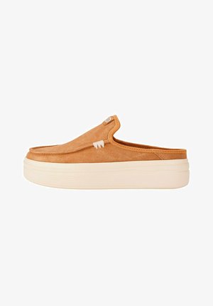 Zapato tipo slip-on en ante marrón con una textura suave, que presenta una costura blanca de acento y una suela gruesa en crema para mayor altura.