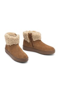 Botas de ante marrón hasta el tobillo con un puño beige esponjoso, cremallera lateral y suela de goma. Textura suave y diseño de punta redonda.