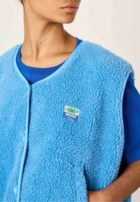 Sinine fliisvest, millel on tekstureeritud pind, kontrastne helesinine äär ja rinnaosas "AMV SUPER VINTAGE" patch.