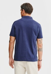 Granatowa koszulka polo z klasycznym kołnierzykiem, krótkimi rękawami i luźnym krojem, wykonana z miękkiej, fakturowanej tkaniny.