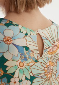 Robe à motif floral avec un col rond et un dos en trou de serrure. Le tissu présente des teintes vives de bleu, vert et orange. Détail de fermeture à bouton inclus.