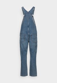 Denimoverall i medelblått, med justerbara axelremmar, v-ringning, flera framfickor och en avslappnad passform. Synliga sömdetaljer.