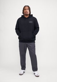 Černá mikina s kapucí a přední kapsou s logem "JACK & JONES", doplněná tmavě šedými cargo kalhotami a bílými teniskami s černými akcenty.