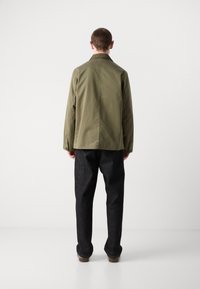 Olive green jacket with a collar, showing a smooth texture. Paired with dark denim pants, featuring a straight leg design and minimal detailing.