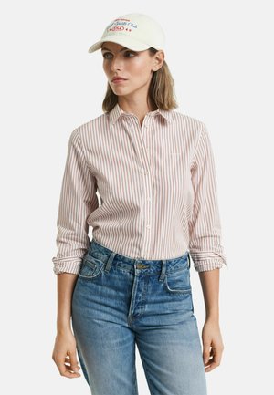 Camicia a righe rossa e bianca, abbinata a jeans in denim blu. Il cappellino è color crema con grafiche ricamate in blu e rosso.