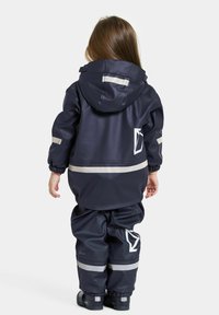 Marine wasserdichte Jacke und Hose mit reflektierenden Streifen. Verfügt über eine Kapuze, elastische Bündchen und große Logo-Akzente auf dem Rücken.