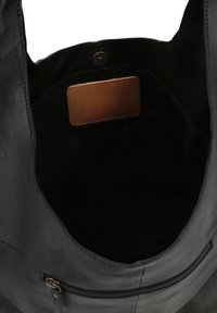 Black leather tote bag with a soft texture, featuring a zippered pocket and a brown leather tag inside. Open-top design for easy access.