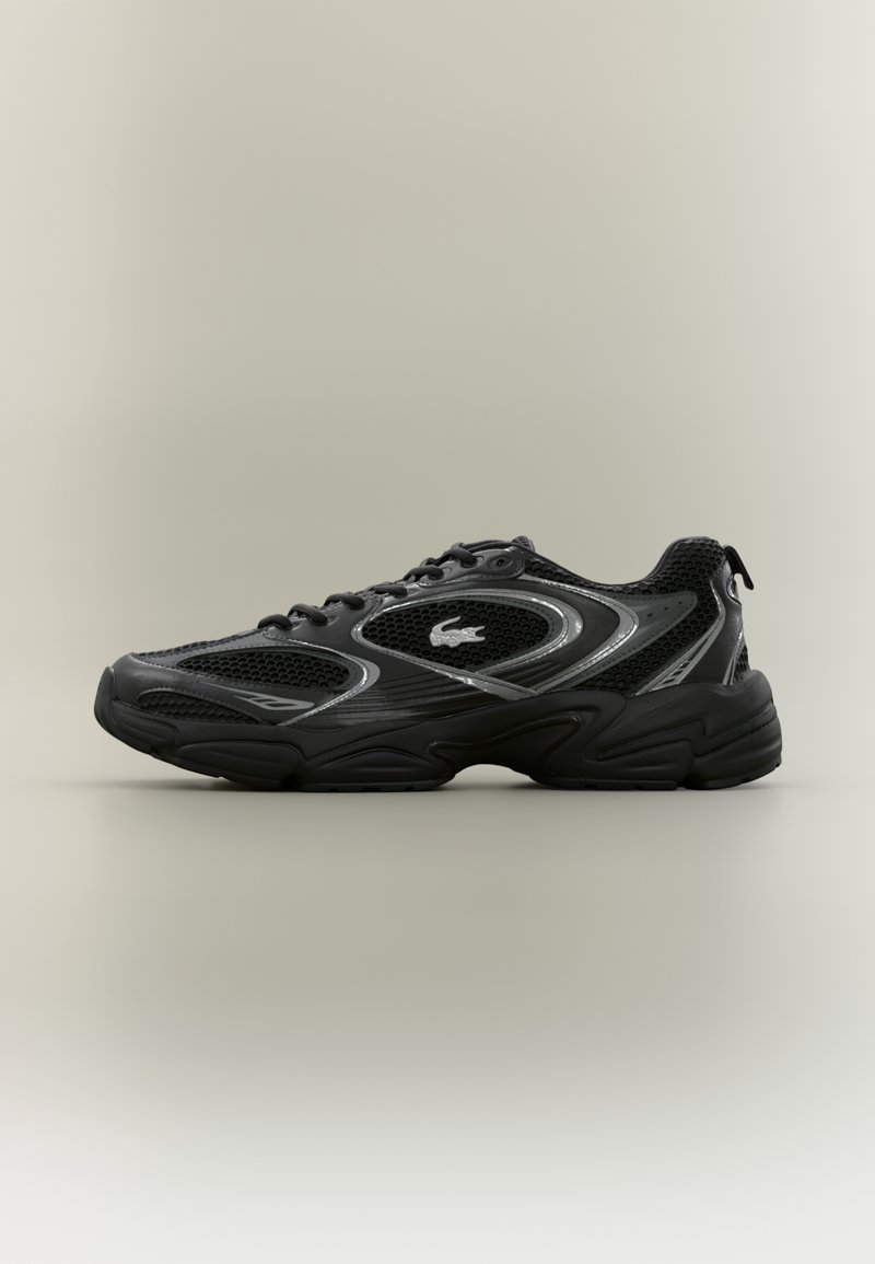 Baskets de sport noires avec panneaux en mesh, semelle épaisse et rembourrée, et un petit logo crocodile sur le côté.