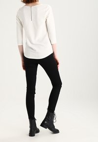 White textured top with a back zipper, three-quarter sleeves, paired with black skinny jeans and black lace-up ankle boots.