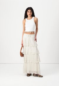 White tank top with a decorative hem, layered polka dot maxi skirt, brown crossbody bag, and leopard print flats. Textured and flowing design.
