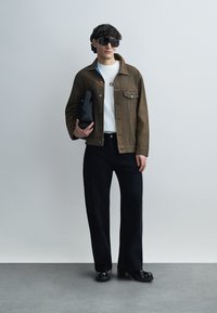 Καφέ τζιν μπουφάν, λευκό μπλουζάκι με τυπωμένο κείμενο, μαύρο τζιν με φαρδιά μπατζάκια και μαύρα παπούτσια με τακούνι. Κρατάει μαύρη τσάντα και φοράει σκουρόχρωμα γυαλιά ηλίου.