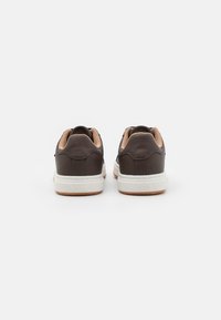 Brune lærersneakers med en tan-interiør, hvite såler og subtil merkevarebygging på baksiden. Har en rund design og rene linjer.