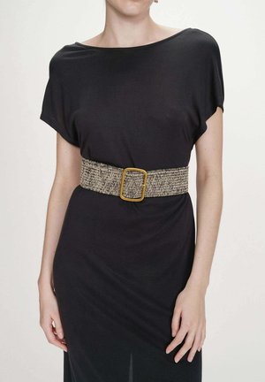 Femme portant une robe noire à manches courtes avec une large ceinture tressée ornée d'une boucle rectangulaire dorée à la taille.