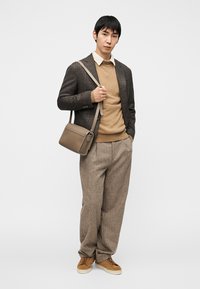 Καφέ καρό σακάκι πάνω από μπεζ πουλόβερ, καφέ παντελόνι και ανοιχτό καφέ αθλητικά παπούτσια. Μικρή καφέ τσάντα χιαστί με φερμουάρ λεπτομέρεια.