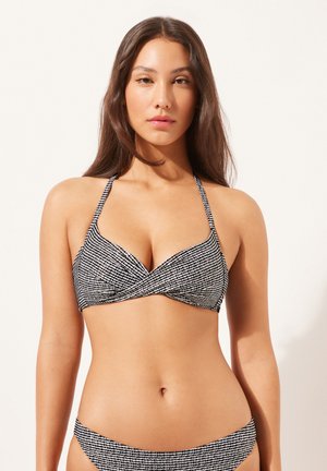 Bikiniöverdel i svart och vitt med mönster, som har en omslagdesign, tunna halterband och en texturerad yta.