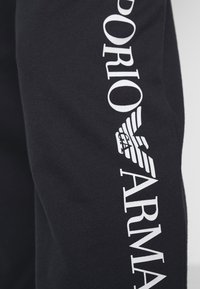 Černá mikina z látky s bílým potištěným nápisem "EMPORIO ARMANI" podél rukávu, obsahující grafické logo s křídly.