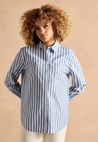 Blue and white striped button-up shirt with long sleeves, collared neck, and curved hem. Made of lightweight fabric with a smooth texture.