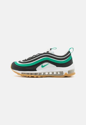 Sneaker bianca e nera con accenti verdi. Presenta un design ondulato, una gomma visibile per l'ammortizzazione e una suola in gomma per la presa. Compresi i lacci e la linguetta.