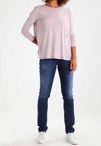 Ljusrosa långärmad skjorta i en lös passform, kombinerad med mörkblå slim fit-jeans och vita sneakers. Mjukt tyg med minimal detaljering.