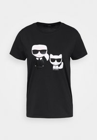 Camiseta de algodón negra con un gráfico blanco de dos figuras de dibujos animados con gafas de sol, una human y un gato, con diseños simples y llamativos.