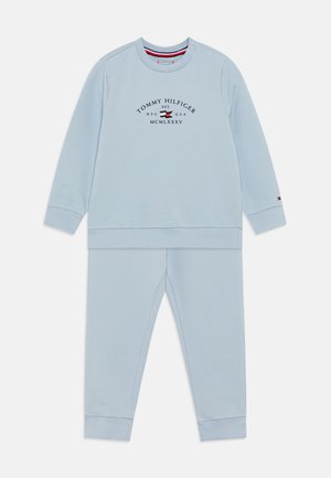 Completo in felpa azzurra chiara composto da felpa e pantaloni realizzati in tessuto morbido. Presenta un collo rotondo, polsini a coste e il logo "Tommy Hilfiger" in blu scuro.