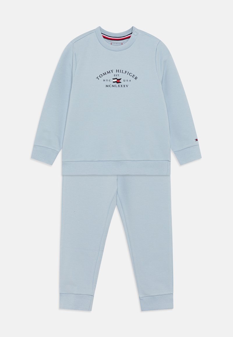 Completo in felpa azzurra chiara composto da felpa e pantaloni realizzati in tessuto morbido. Presenta un collo rotondo, polsini a coste e il logo "Tommy Hilfiger" in blu scuro.