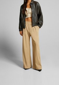 Černá kožená bomber bunda, béžové plisé široké kalhoty s plisováním a těsně přiléhající krémový žebrovaný krátký top. Hladká struktura s výraznými tvary.