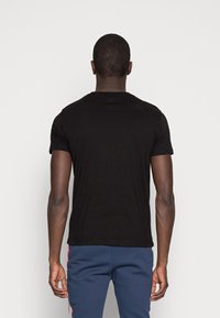 Schwarzes Baumwoll-T-Shirt mit kurzen Ärmeln und Rundhalsausschnitt, von hinten betrachtet. Glatte Textur ohne sichtbare Muster oder Akzente.