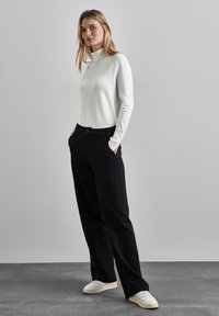 Weißer langärmliger Rollkragenpullover kombiniert mit schwarzen, hoch taillierten Hosen und weißen Sneakers; glatte Texturen, tailliert, gerades Bein-Design.