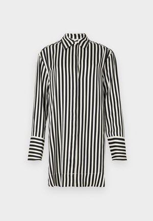 Camisa de rayas en blanco y negro con cuello puntiagudo, mangas largas y cierre frontal con botones. Presenta rayas anchas y estrechas alternadas.