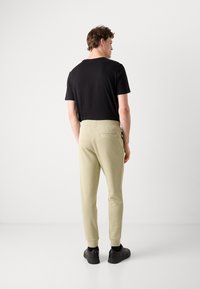 Light beige joggers with a slim fit, elastic waistband, and a back pocket. Worn with a black t-shirt and black sneakers.