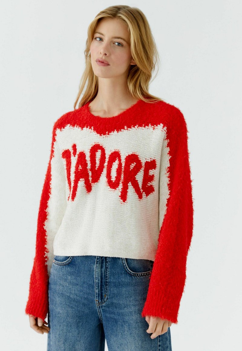 Rode en witte gebreide trui met de tekst "J'ADORE" in een vetgedrukt lettertype. Heeft een cropped ontwerp met lange, losse mouwen en een ronde hals.