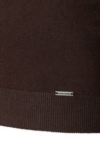 Brauner gestrickter Pullover mit ribbenförmigem Saum und einem kleinen silbernen Logoetikett, das mit "MORE & MORE" zur Markenidentifikation beschriftet ist.