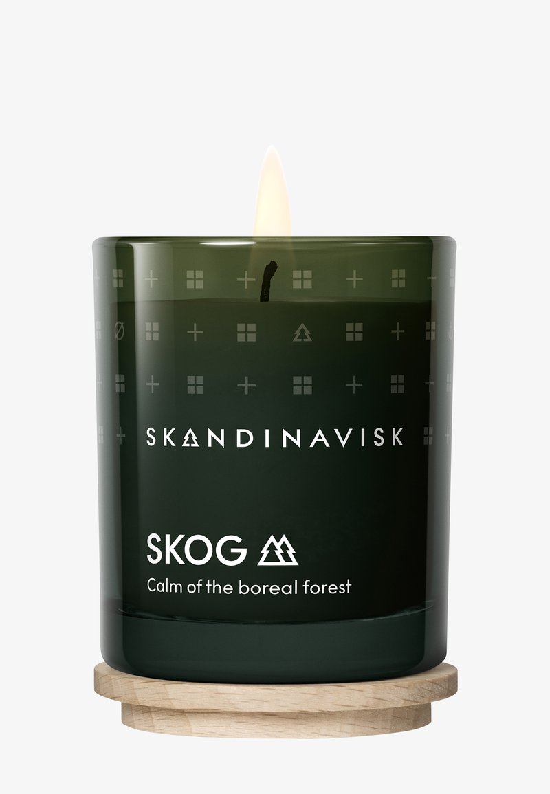 Green glass candle with a glowing flame. Textured surface featuring geometric patterns. Label reads “SKOG, Calm of the boreal forest.” Wood base.
