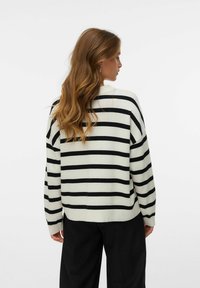 Gestreifter Oversized-Pullover mit schwarzen Streifen auf cremefarbenem Hintergrund, mit Rundhalsausschnitt und überschnittenen Schultern. Weiche Stricktextur.