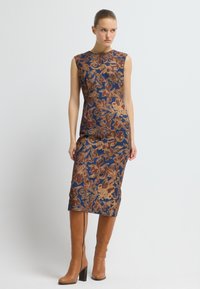 ÄrmARLÖS midi-klänning med en blå bas och bruna blommönster. Kombinerad med knähöga bruna läderstövlar och blockklack.