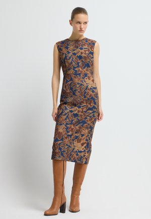 Mouwloze midi-jurk met een blauwe basis en bruine bloemenpatronen. Gecombineerd met kniehoge bruine leren laarzen met blokhakken.