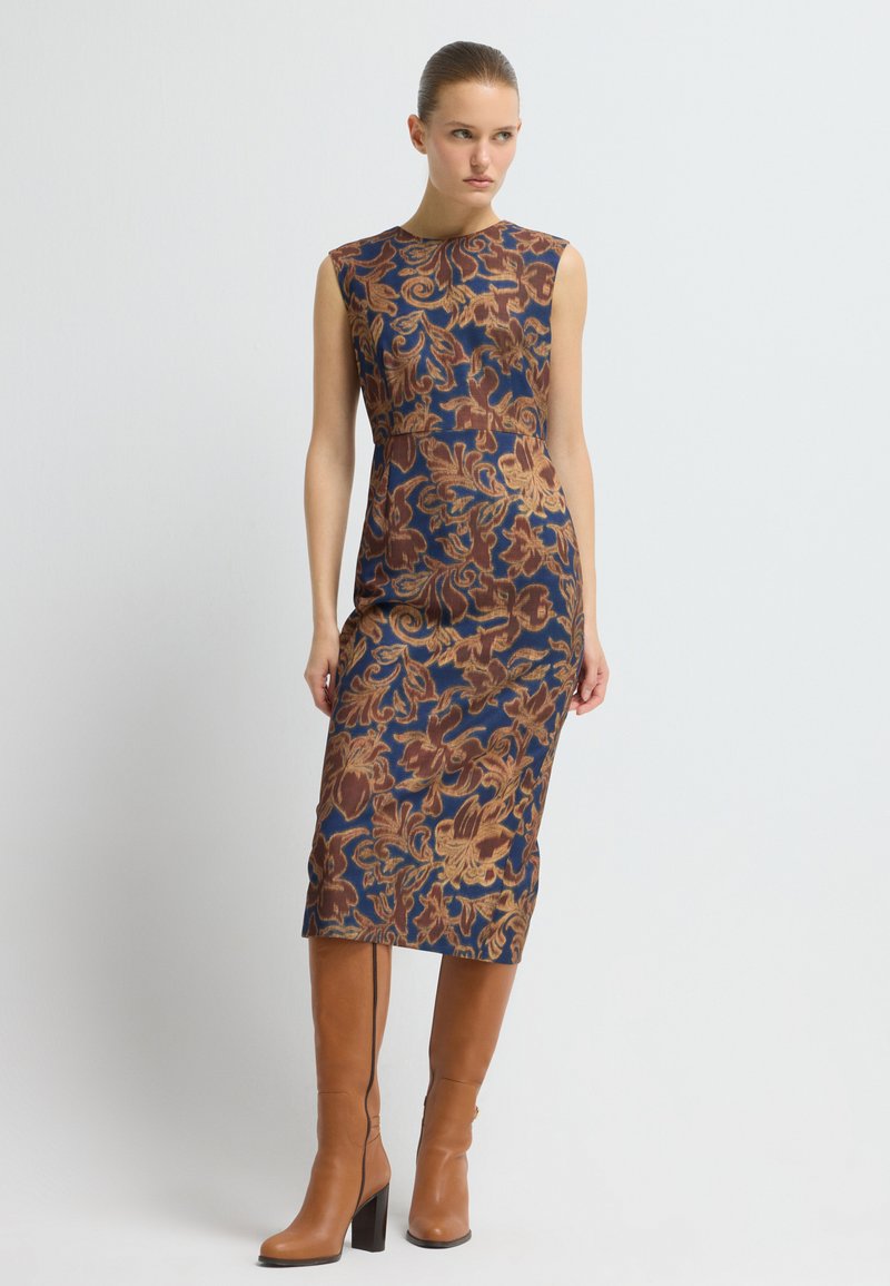 ÄrmARLÖS midi-klänning med en blå bas och bruna blommönster. Kombinerad med knähöga bruna läderstövlar och blockklack.