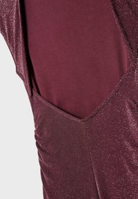 Primo piano di un tessuto viola scuro scintillante con una texture arricciata e una fodera liscia viola solido sottostante.