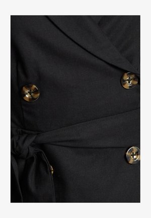 Zwarte wikkeljurk met een gestrikte taille en grote ronde knopen met een tortoisepatroon. De stof lijkt glad met een lichte glans.