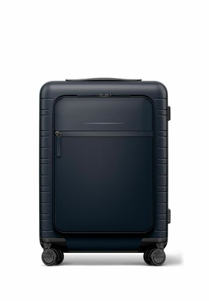 Compact black hard-shell suitcase with front zip pocket and four swivel wheels, shown upright on a white background.