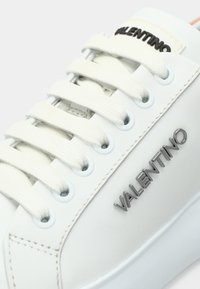 Λευκό δερμάτινο αθλητικό παπούτσι με επίπεδες, υφαντές κορδόνια, ασημένια μεταλλικά στοιχεία για τη σήμανση και στρογγυλές τρύπες. Ομαλή υφή με μινιμαλιστικό σχεδιασμό.