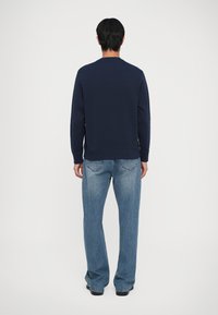 Sweatshirt azul-marinho de mangas longas e gola redonda, combinado com jeans de ganga de perna larga azul-claro, visto pela parte de trás.