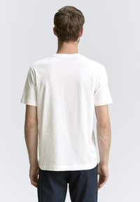 Camiseta corta de algodón blanca con cuello redondo y textura lisa y sencilla, mostrada desde la parte de atrás sin logotipos visibles.