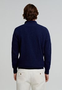 Mørkeblå strikket pullover med lange ærmer og krave. Glat tekstur, ribbede manchetter og kant. Model vist fra ryggen, iført lyse bukser.