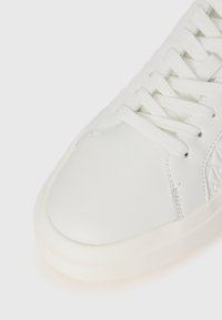Adidas alb cu o suprafață din piele netedă, vârf rotund și șireturi albe. Dispune de o textură subtilă pe lateral și o talpă groasă din cauciuc.