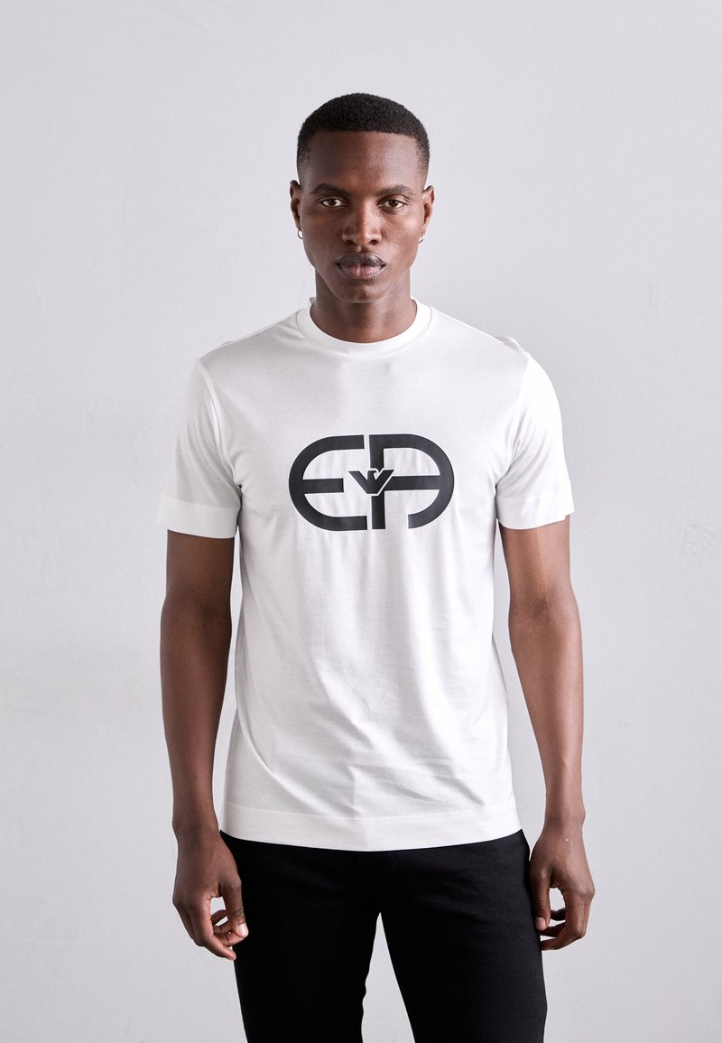 Tricou alb cu mânecă scurtă, din bumbac, având un logo mare imprimat în negru pe partea din față. Design simplu, cu gât rotund.