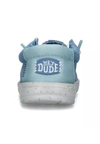 Sneaker in tela blu chiaro con superficie testurizzata, caratterizzata da una toppa bianca con il logo "HEY DUDE" e una suola bianca con macchie.