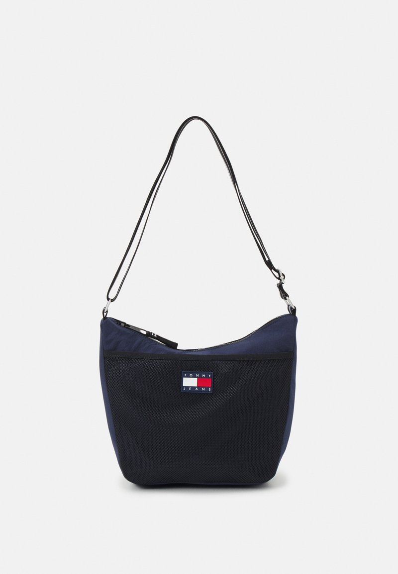 Navy nylon shoulder bag with a mesh front, zip closure, and adjustable strap. Features a Tommy Jeans logo patch in red, white, and blue.